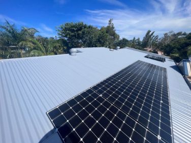 Solar Panels on a Gray Corrugated Metal Roof Under a Bright Blue Sky — Rumara Roofing in Sunshine Coast, QLD