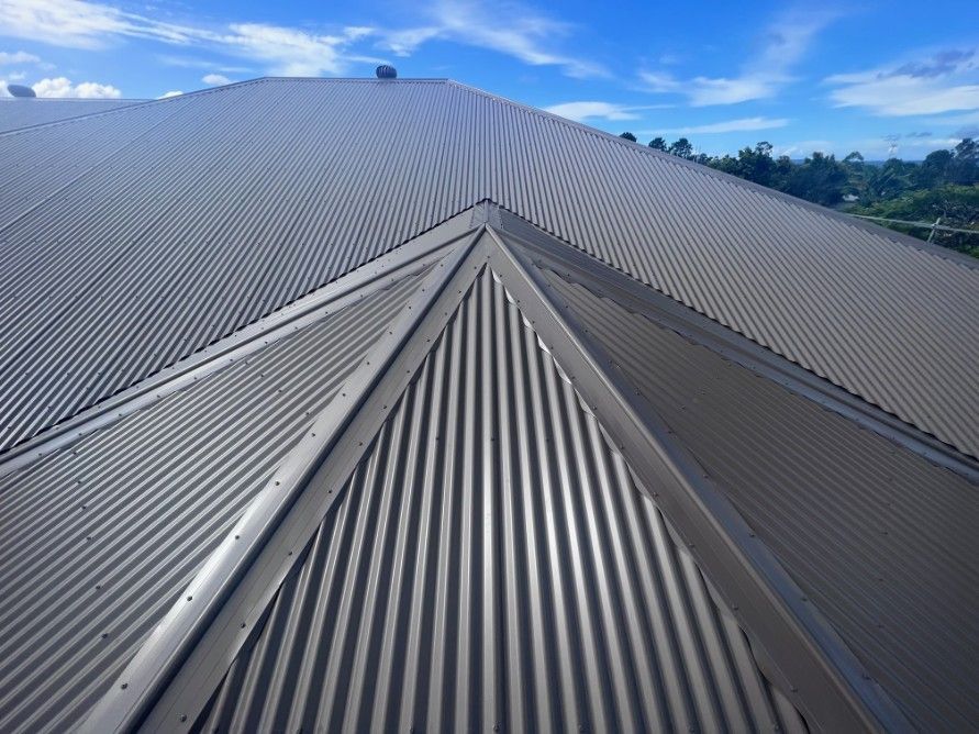 Gray Corrugated Metal Roof With a Triangular Design Against a Bright Blue Sky — Rumara Roofing in Sunshine Coast, QLD