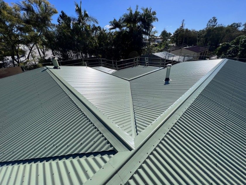 Green Corrugated Metal Roof on a House With Vents, Visible Trees and Blue Sky — Rumara Roofing in Maryborough, QLD