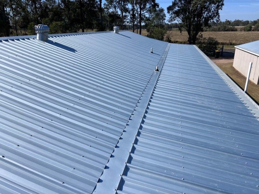 Blue Corrugated Metal Roof of a Building, With Vents and Trees in the Background — Rumara Roofing in Maryborough, QLD