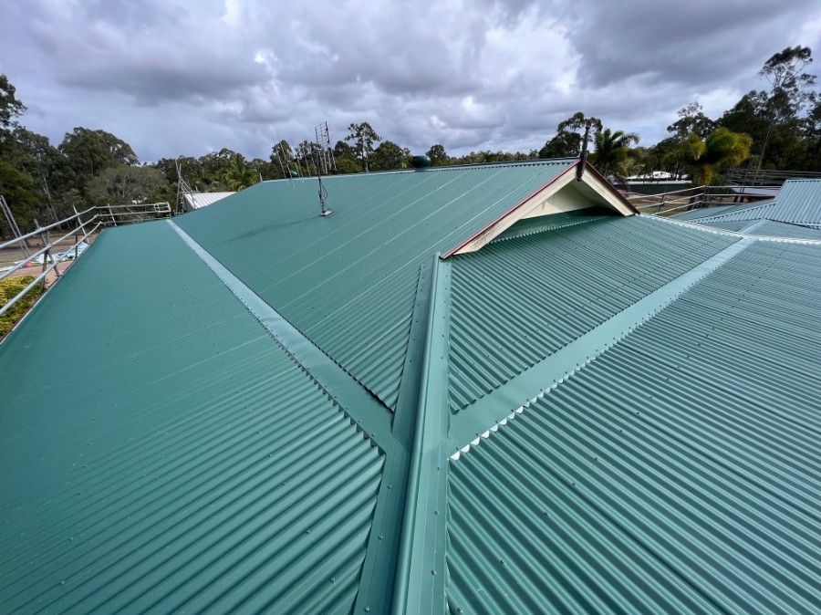 Green Corrugated Metal Roof on a Building Under a Cloudy Sky — Rumara Roofing in Nambour, QLD