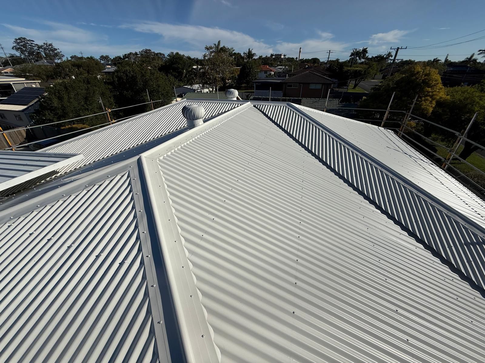 White corrugated metal roof with safety railing under a blue sky — Rumara Roofing in Sunshine Coast, QLD