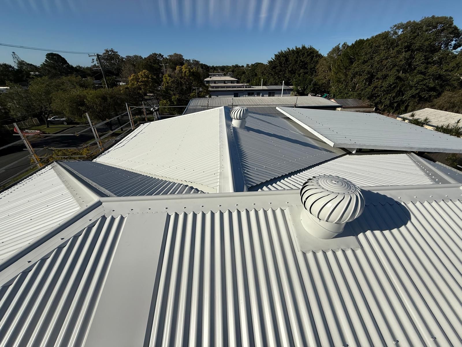 White corrugated metal roof with vent and other structures against a blue sky — Rumara Roofing in Sunshine Coast, QLD