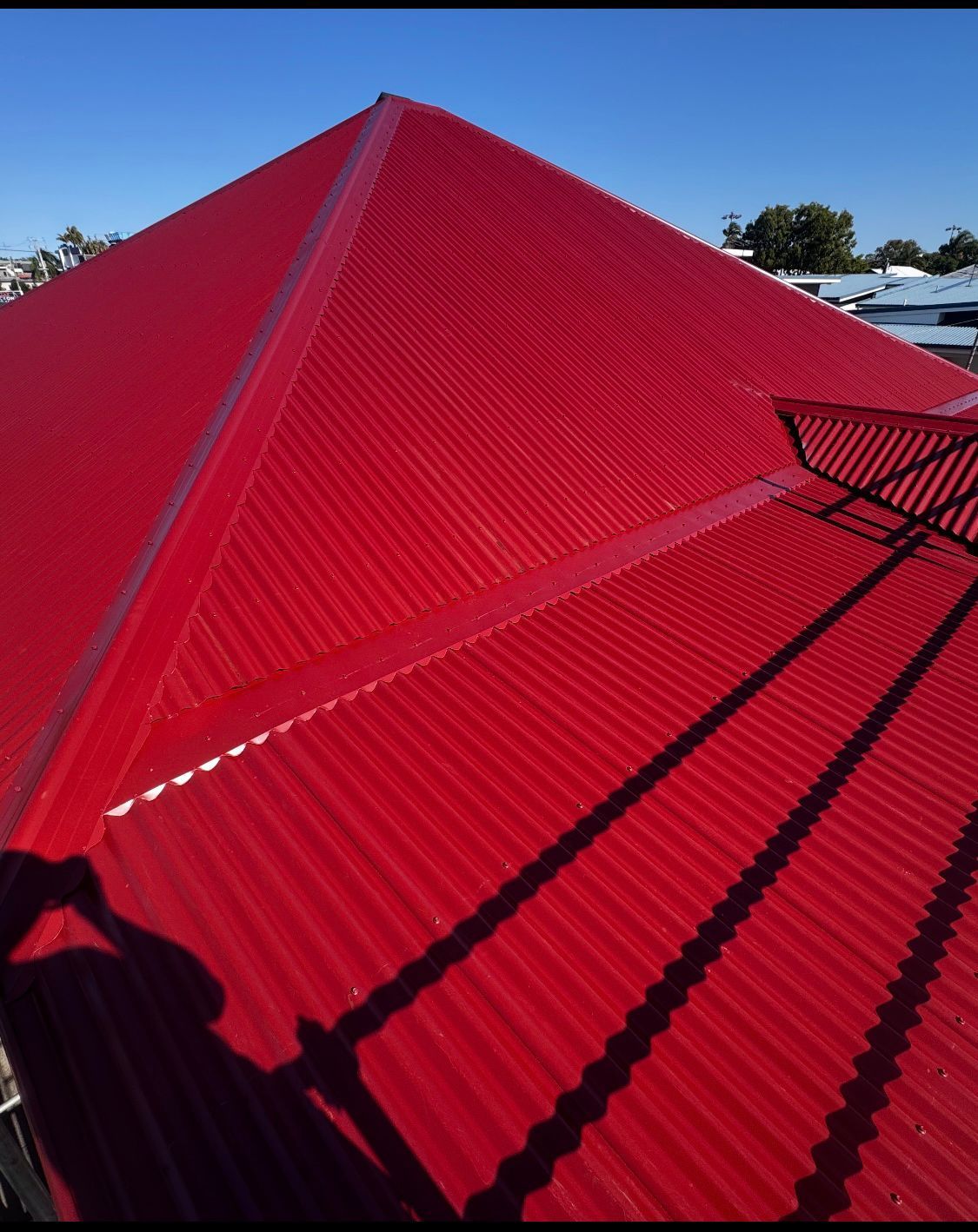 Red corrugated metal roof under a blue sky, with ridgeline and shadows visible — Rumara Roofing in Sunshine Coast, QLD