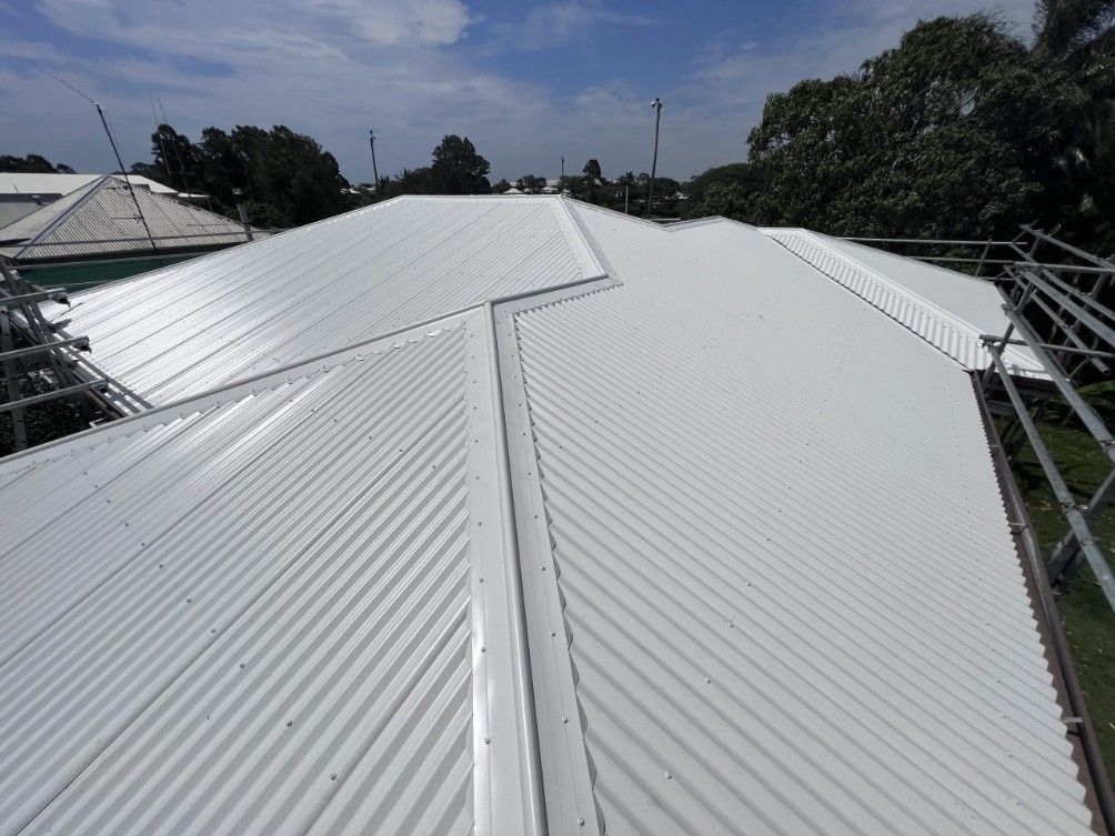 White Corrugated Metal Roof on a Building Against a Blue Sky With Trees — Rumara Roofing in Sunshine Coast, QLD
