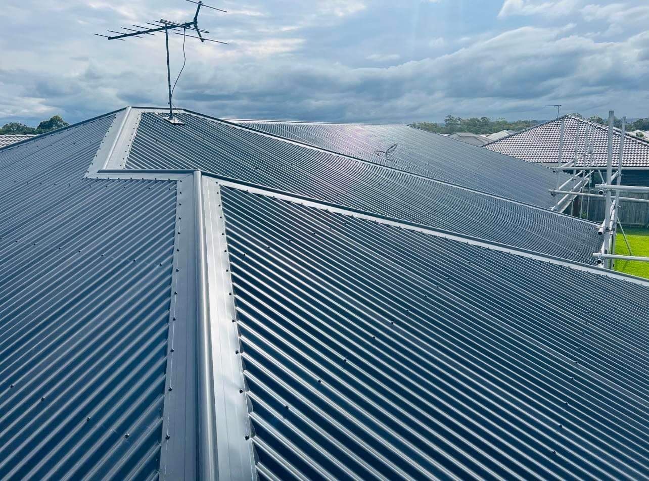 Gray Corrugated Metal Roof With an Antenna, on a House Under a Cloudy Sky — Rumara Roofing in Sunshine Coast, QLD