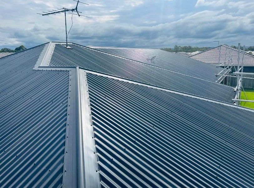 Gray Corrugated Metal Roof With Antenna, Angled Against a Cloudy Sky — Rumara Roofing in Maroochydore, QLD