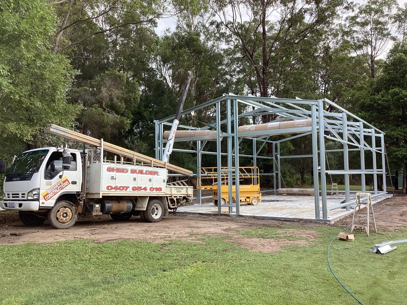 White Truck Beside a Steel Building Frame on A Grassy Construction Site — Bridgey's Constructions in Wallabi Point, NSW