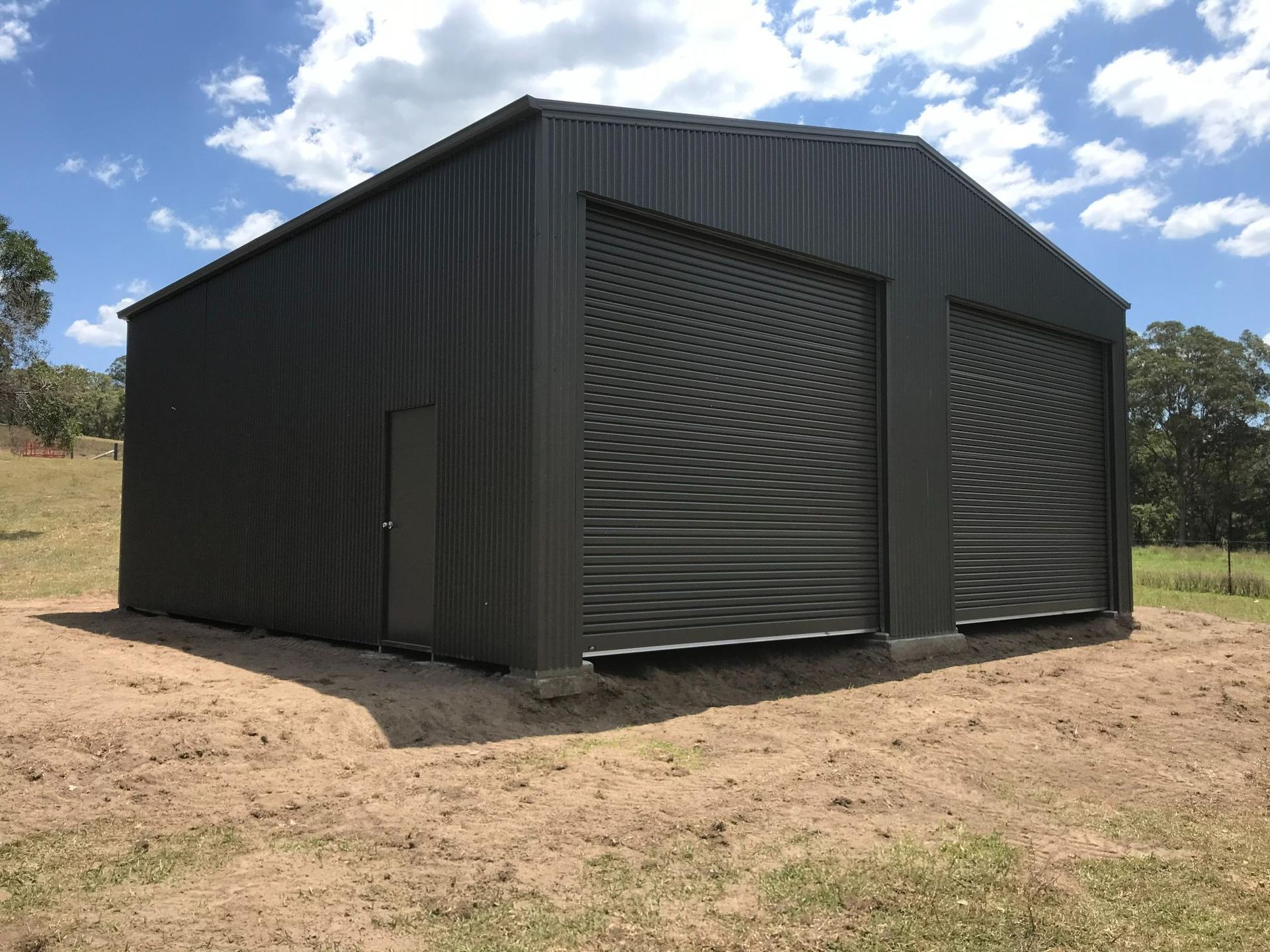 Black Metal Shed with Large Roll Up Doors on A Dirt Lot — Bridgey's Constructions in Diamond Beach, NSW