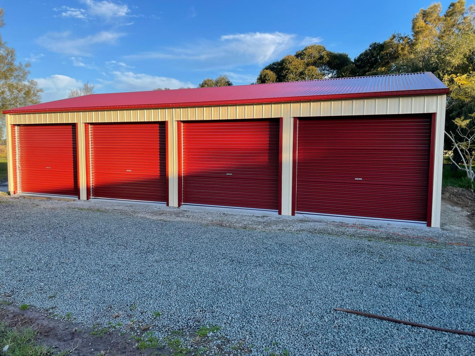 Four Red Storage Unit Doors in A Gravel Lot Under a Blue Sky — Bridgey's Constructions in Diamond Beach, NSW