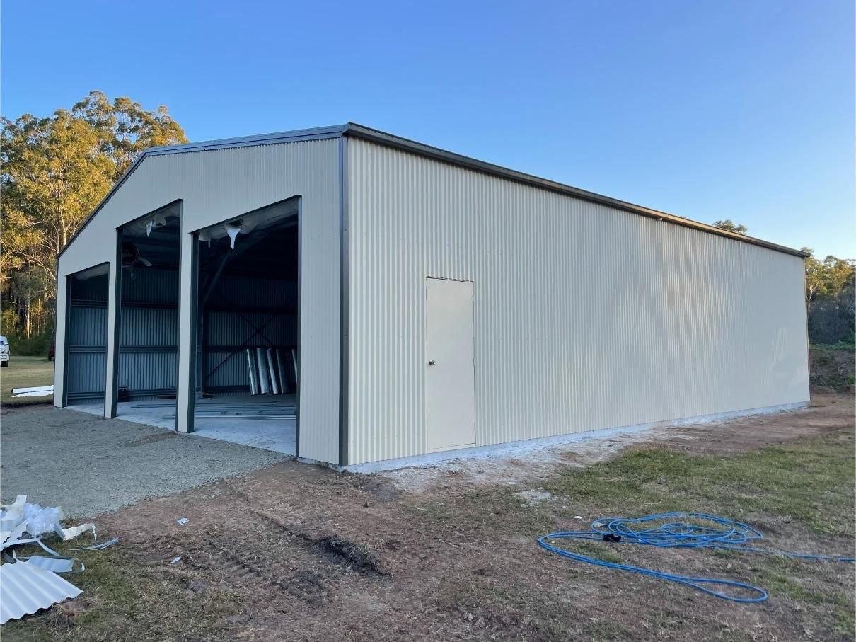 Large Tan Metal Shed With Three Garage Bays and a Side Door — Bridgey's Constructions in Port Macquarie, NSW