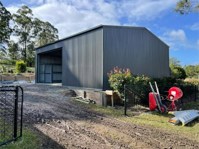 Dark Grey Metal Shed With an Open Front Door on a Gravel Driveway — Bridgey's Constructions in Pacific Palms, NSW