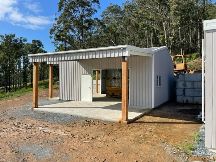 A Light Grey Metal Shed With Two Garage Doors and a Side Door Sits on a Gravel Driveway  — Bridgey's Constructions in Wallabi Point, NSW