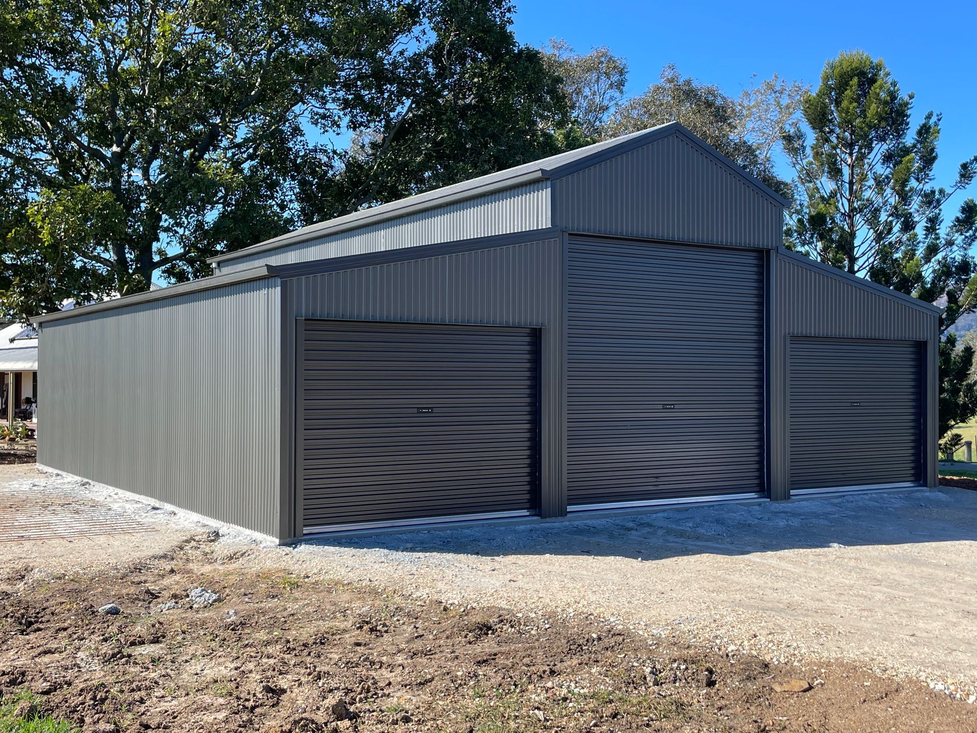 Large Gray Metal Storage Building with Roll Up Doors on A Gravel Lot — Bridgey's Constructions in Diamond Beach, NSW