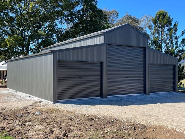 Gray Metal Storage Shed with Roll Up Doors on A Gravel Lot — Bridgey's Constructions in Wallabi Point, NSW
