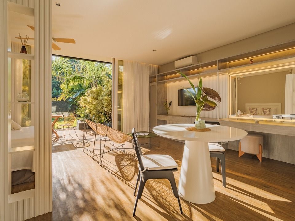 Sala de jantar ampla e ensolarada com mesa redonda branca, cadeiras, portas de correr para o pátio e vista para o jardim.