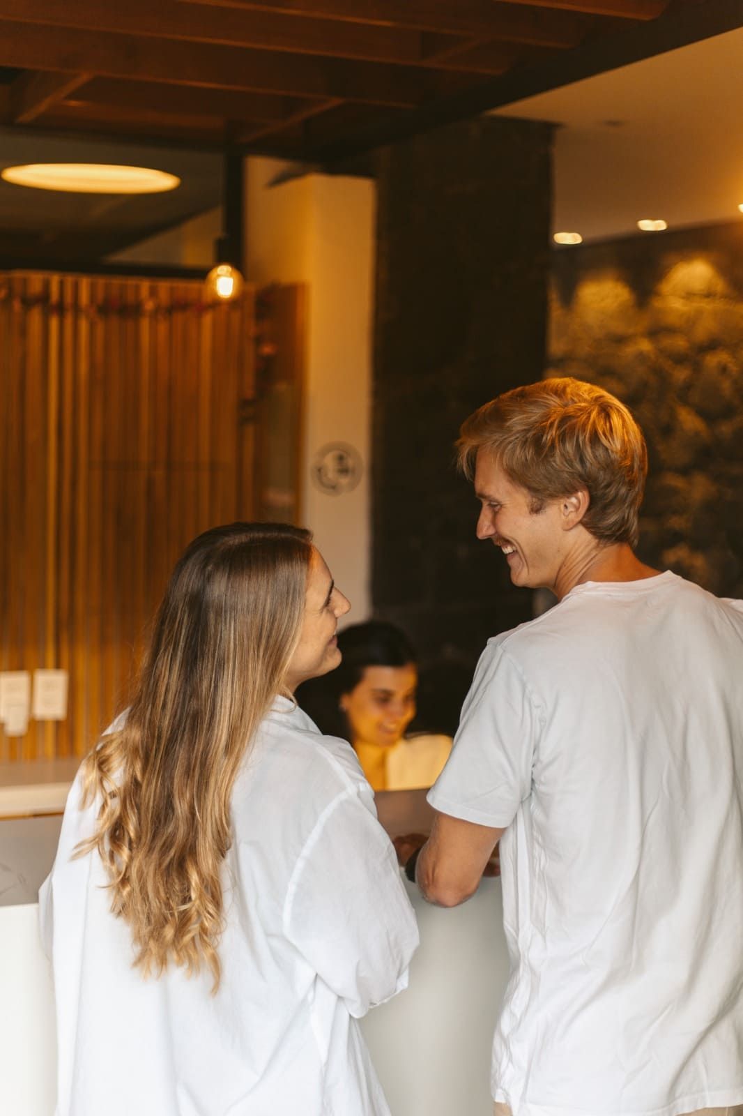 Duas pessoas de camisa branca conversando em um café ou restaurante com iluminação aconchegante.
