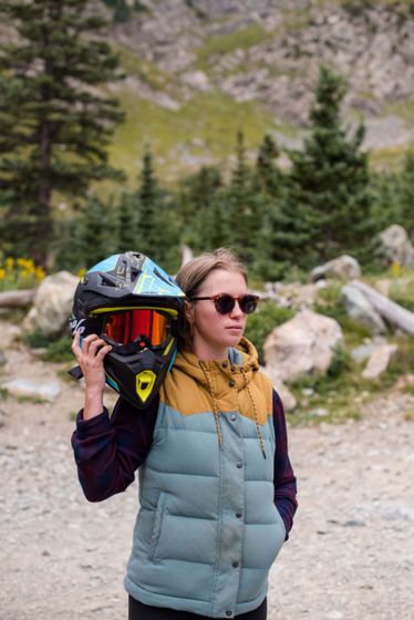 A woman is carrying a helmet and goggles on her back.