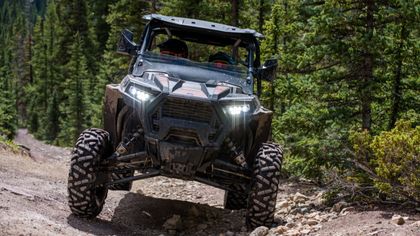 A man is driving a polaris rzr 1000 atv on a dirt road.