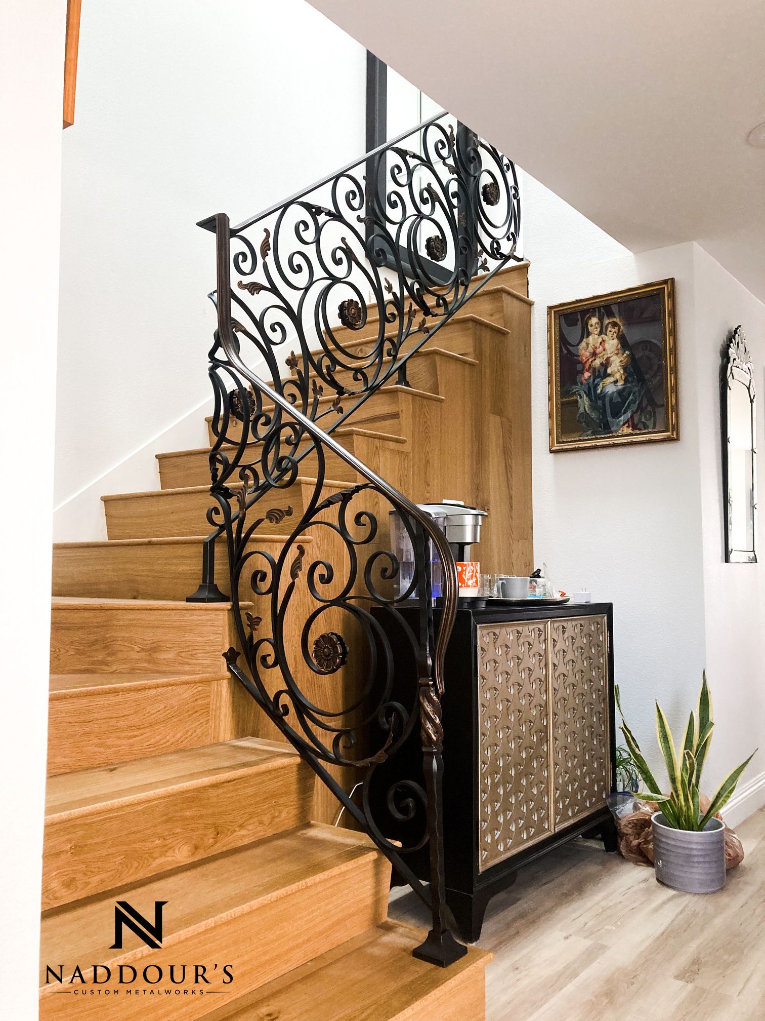 A wooden staircase with a wrought iron railing and a painting on the wall.