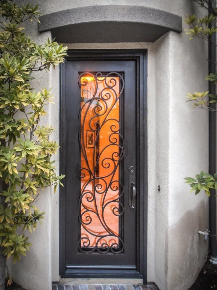 A black door with a wrought iron design on it is surrounded by trees.