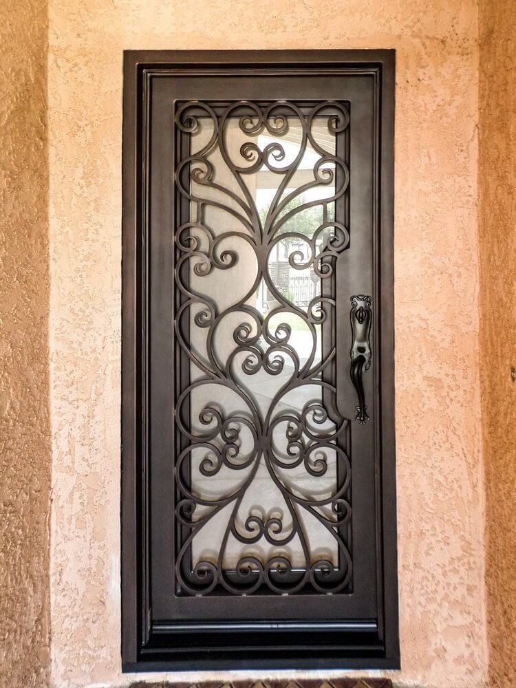 A black door with a wrought iron design on it is on a white wall.