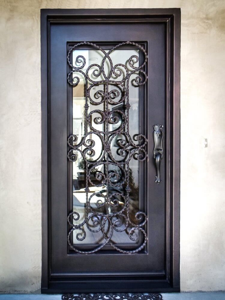 A wrought iron door with a glass window is on a white brick wall.