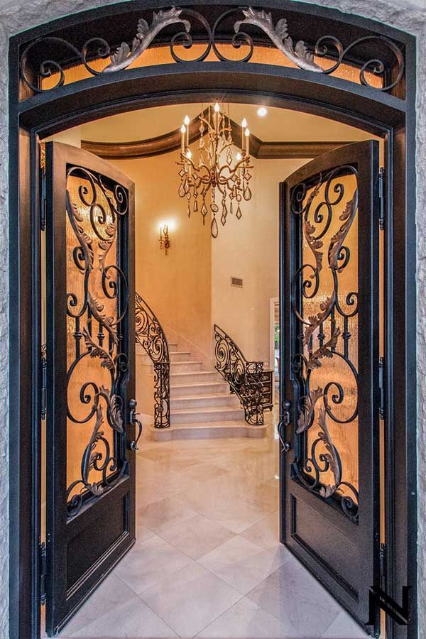 A wrought iron door is open to a hallway with stairs and a chandelier.