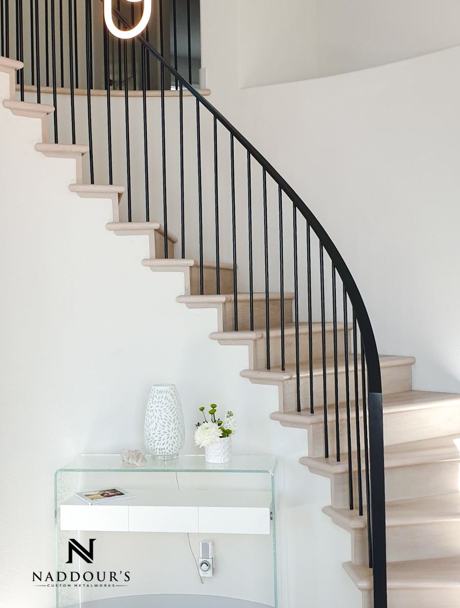 A curved staircase with a black railing and a white wall.