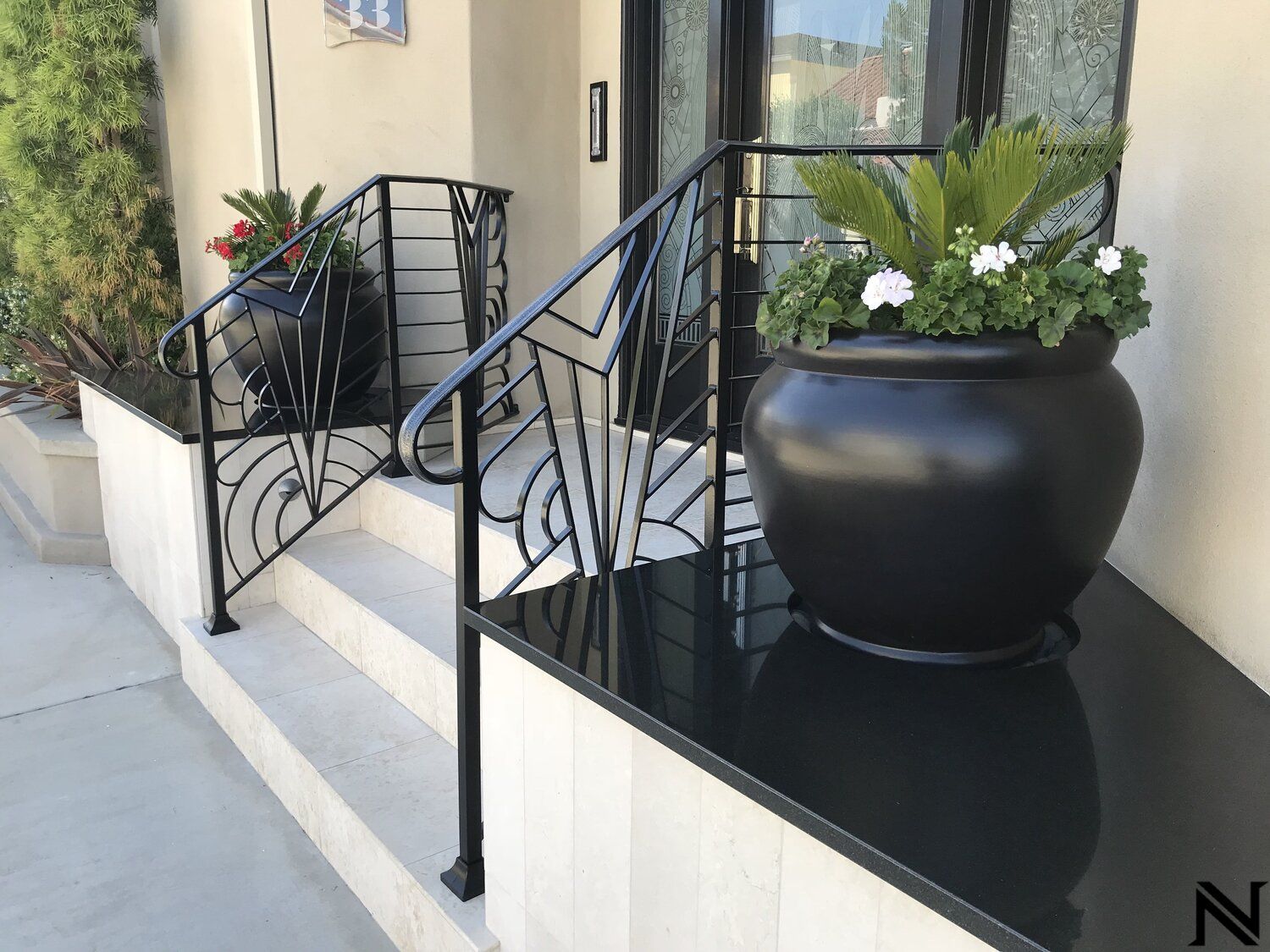 A black potted plant is sitting on a black counter next to a wrought iron railing.