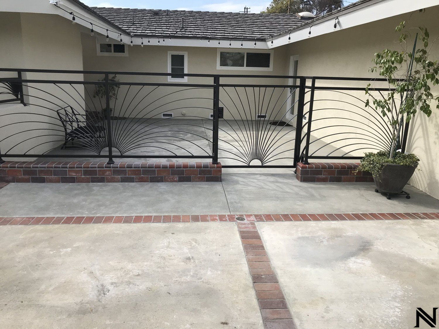 A wrought iron fence surrounds a driveway in front of a house.