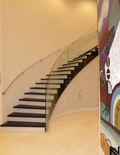 A curved staircase with a glass railing and a painting on the wall behind it