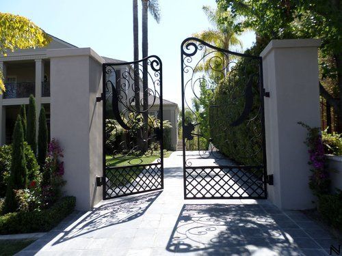 A wrought iron gate is open to a driveway leading to a house