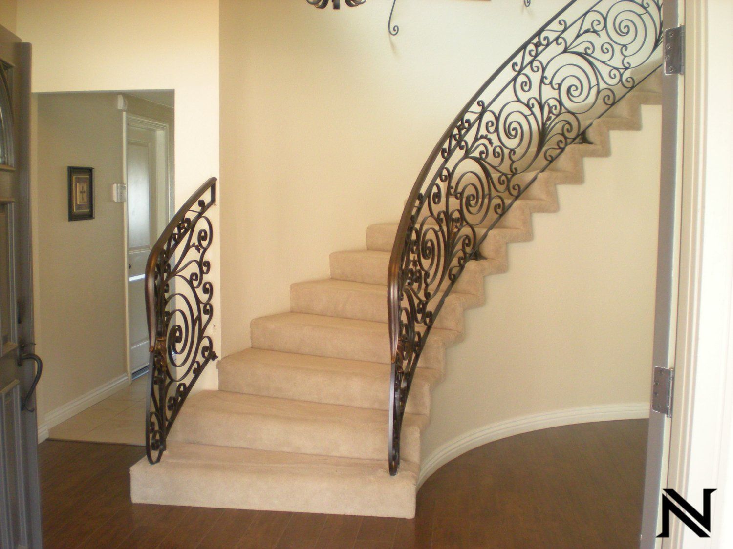 A curved staircase with a wrought iron railing and the letter n in the corner