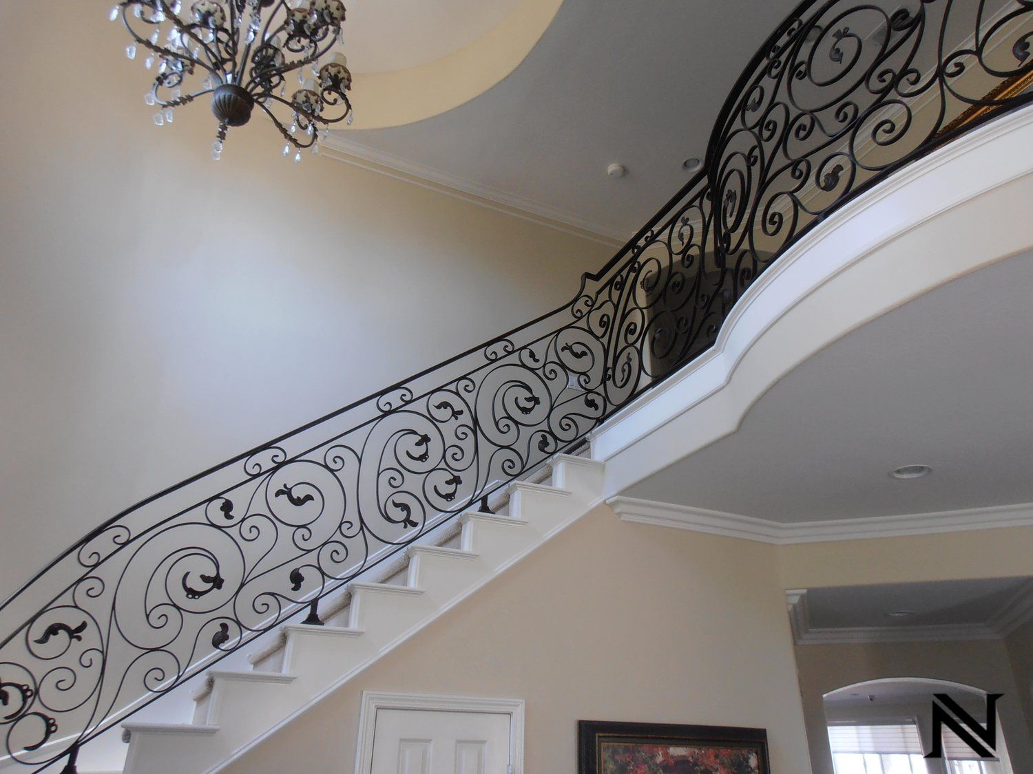 A staircase with a wrought iron railing and a chandelier hanging from the ceiling
