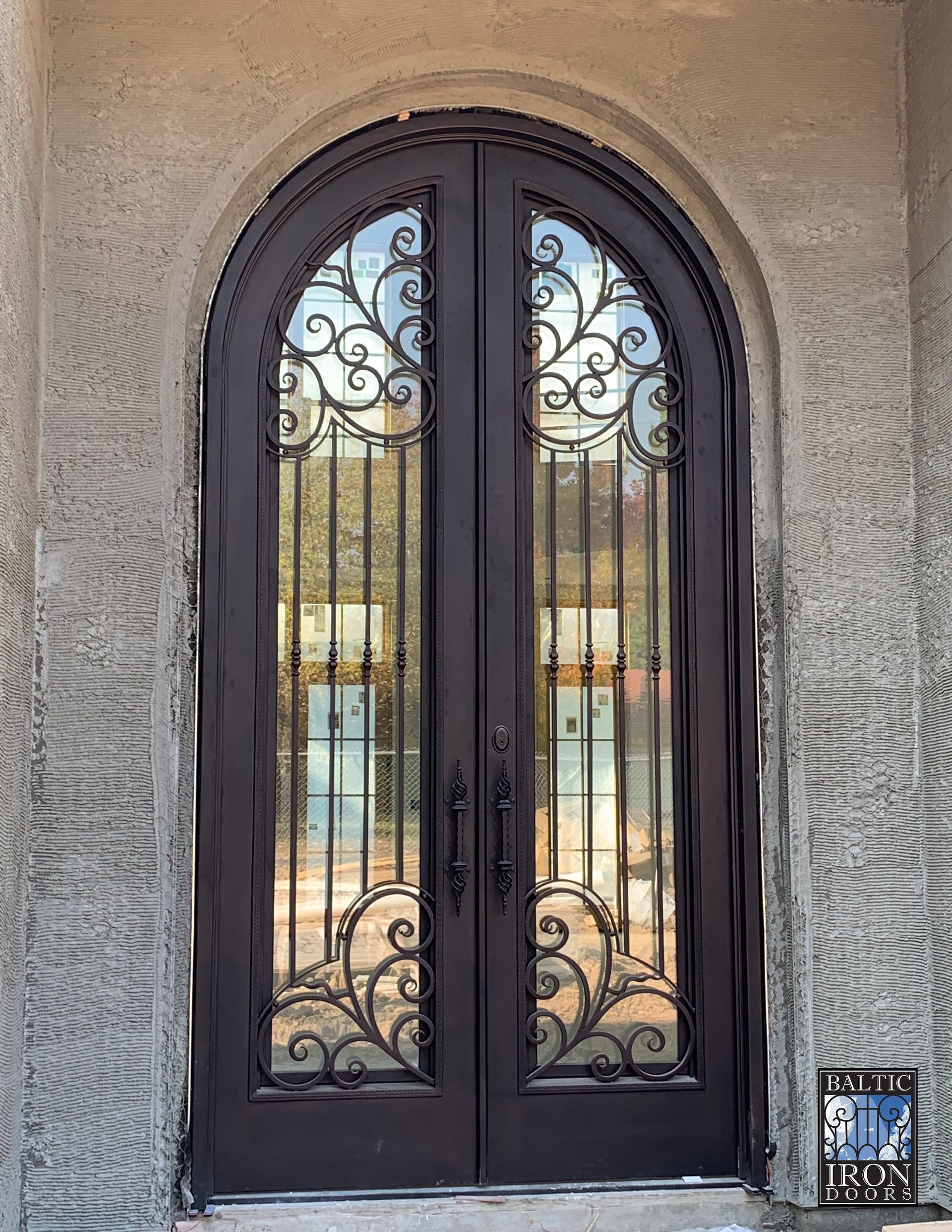 A pair of arched wrought iron doors on a stone wall.