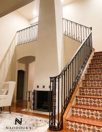 A staircase with a wrought iron railing and a fireplace with naddour 's written on the bottom