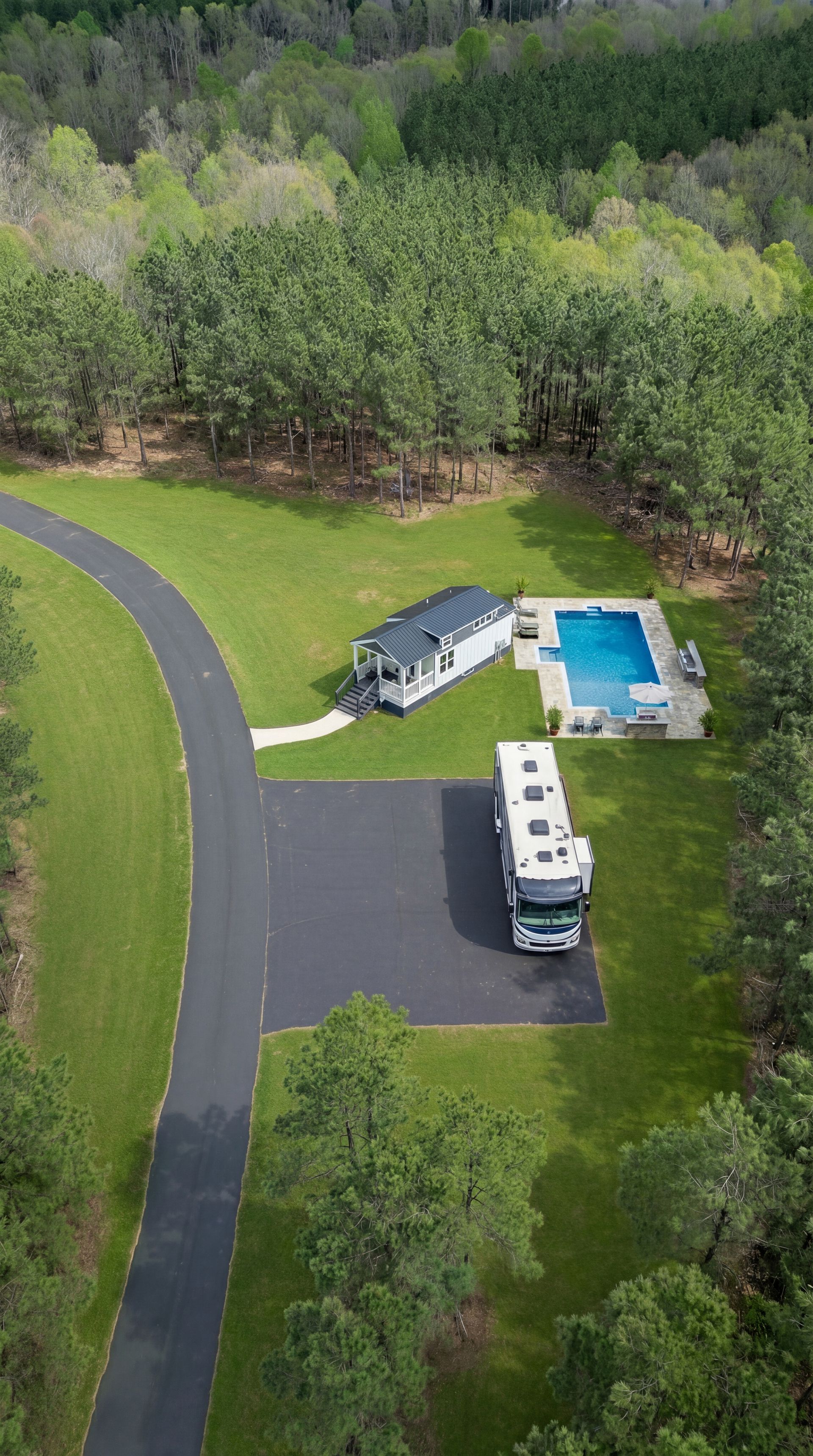Aerial view of a white RV parked beside a house with a blue pool, surrounded by trees.