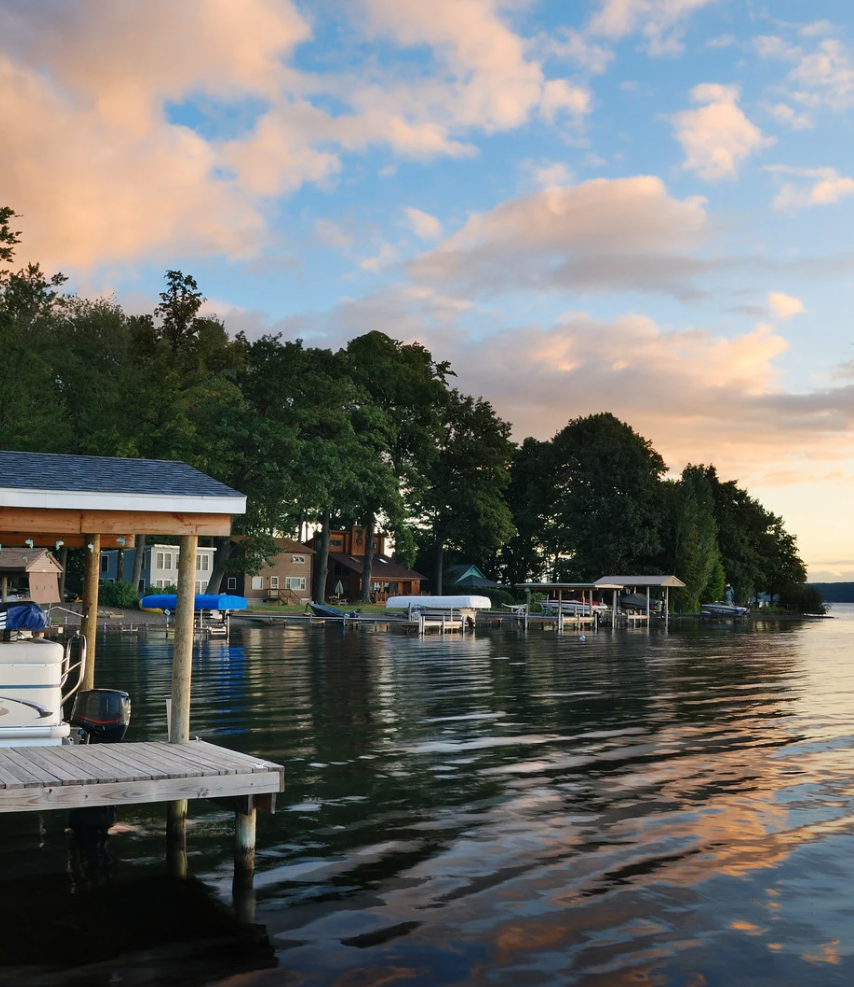 Sunset over a calm lakeside dock with boats, trees, and reflections on the water