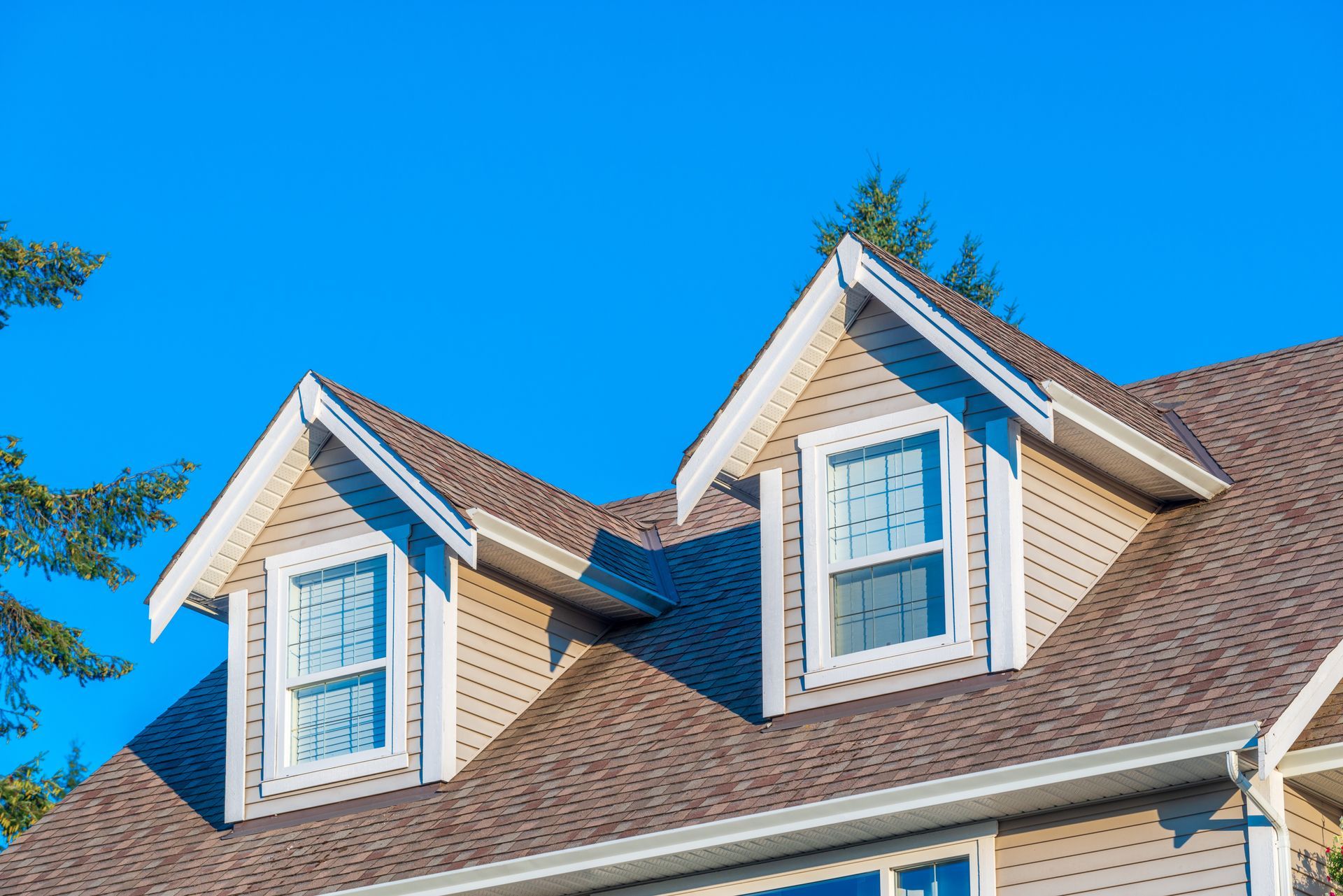 Dormer windows with white trim on a shingled house under a bright blue sky