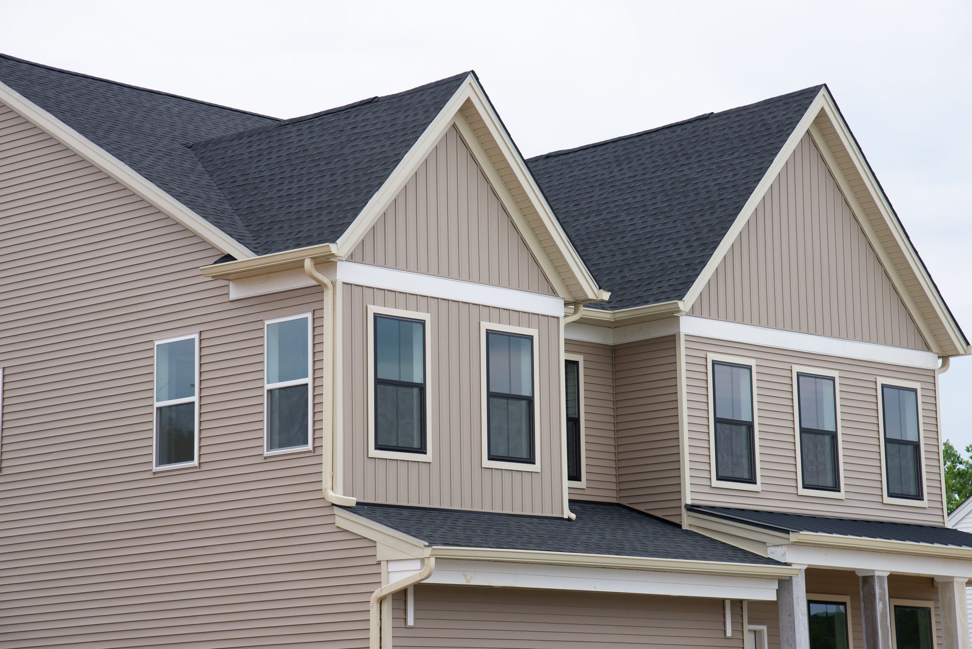 Two-story beige suburban house with gray roof and tan trim, seen from the front-left angle