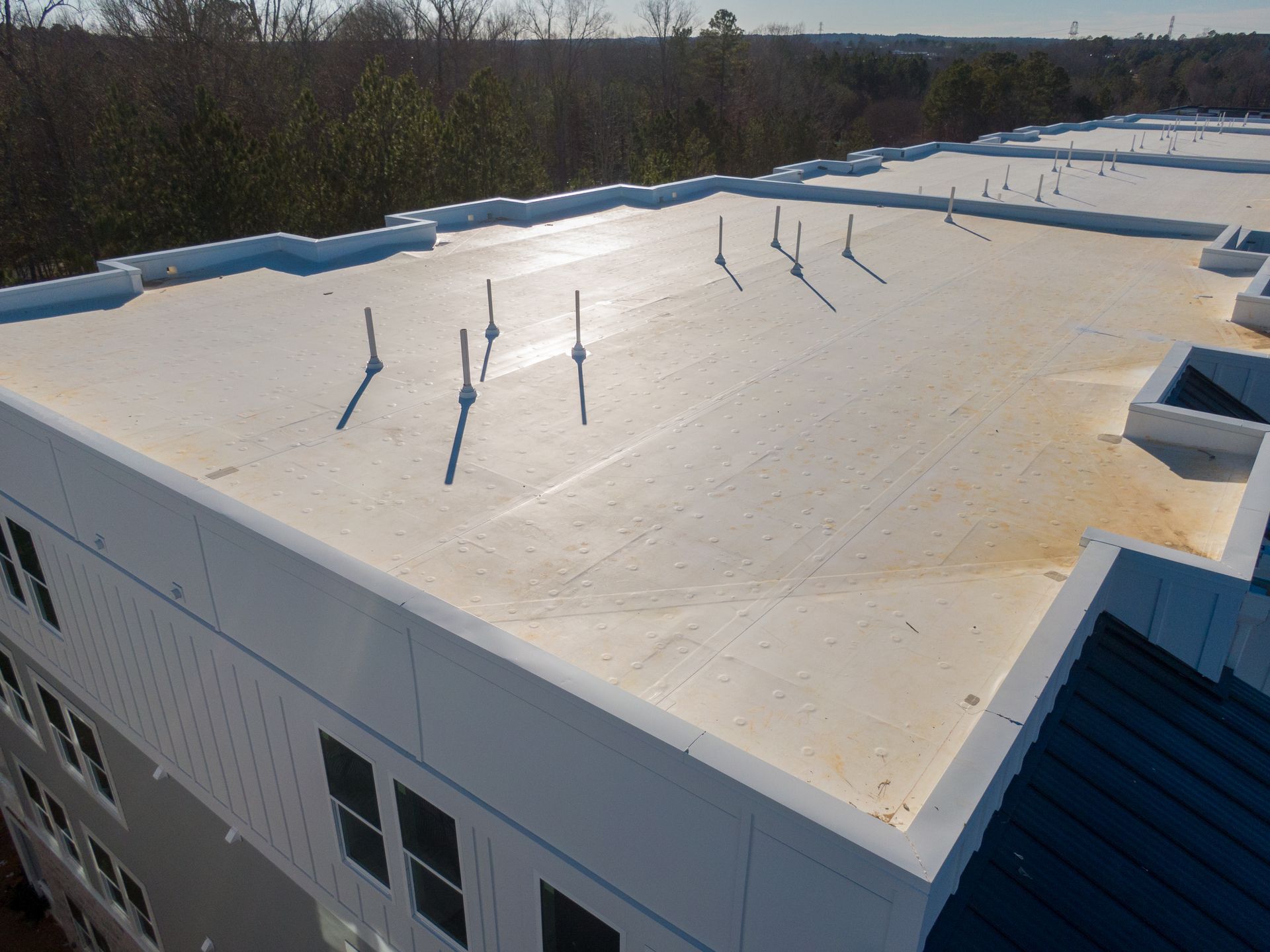 White flat-roofed building under construction with rooftop vents and blue trim, viewed from above