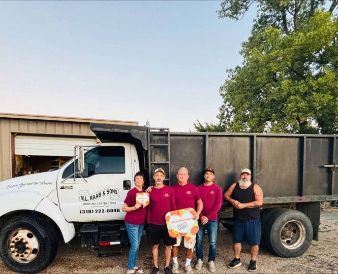 Five people pose beside a white truck and black dump trailer in a gravel lot.