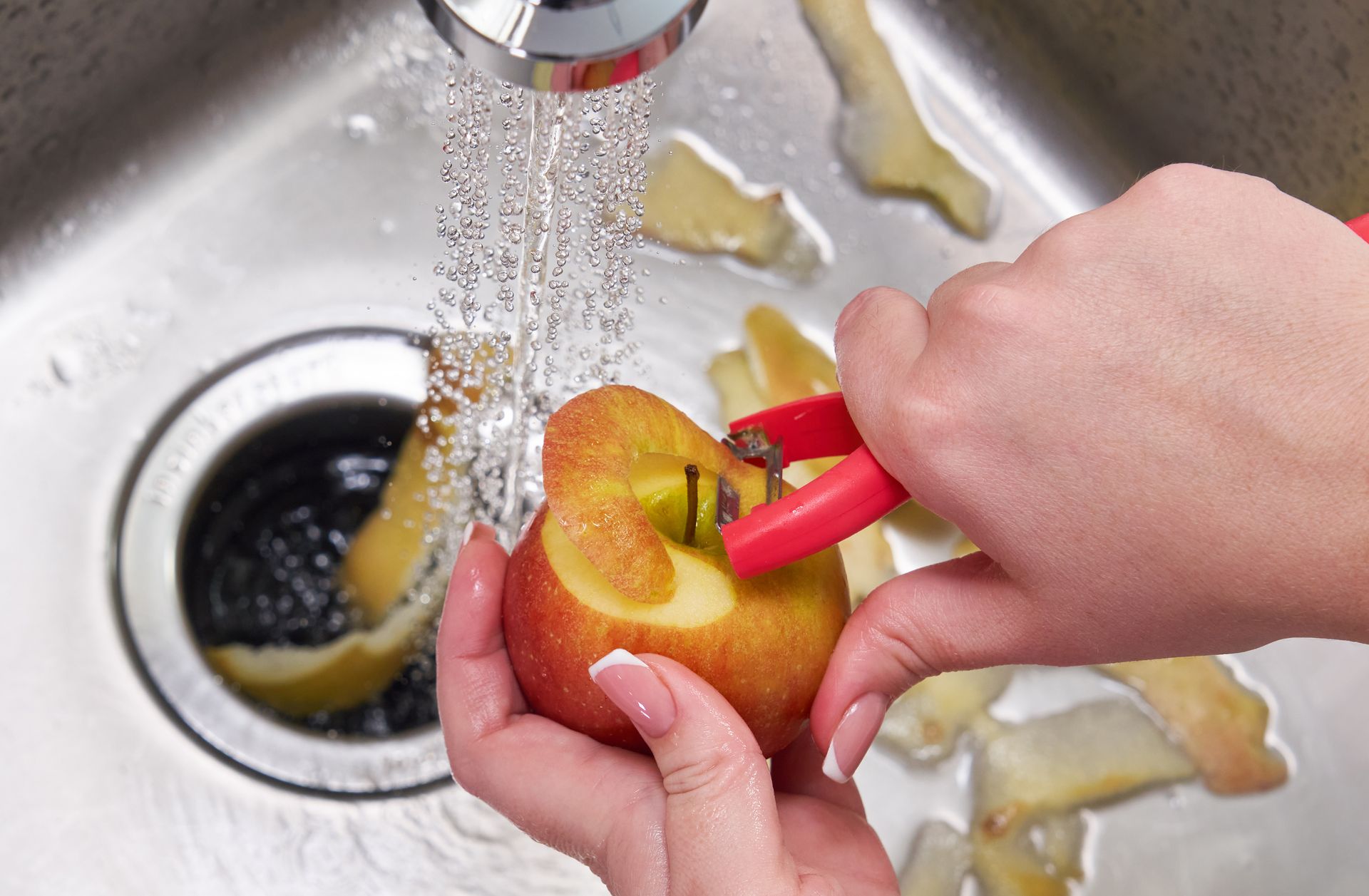 A person is peeling an apple in a sink.