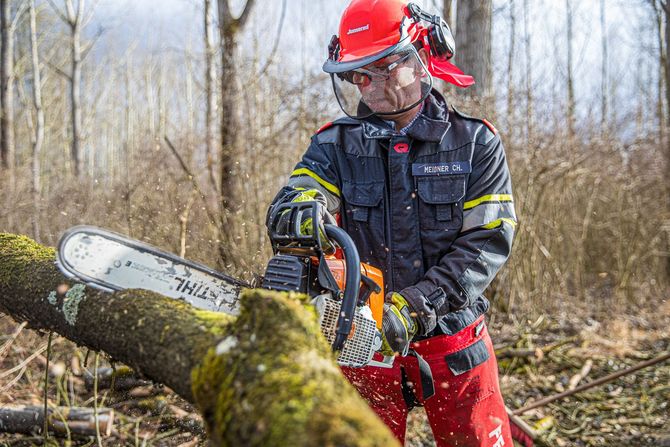Chainsaw operator in red helmet and protective gear cutting a log in a wooded area