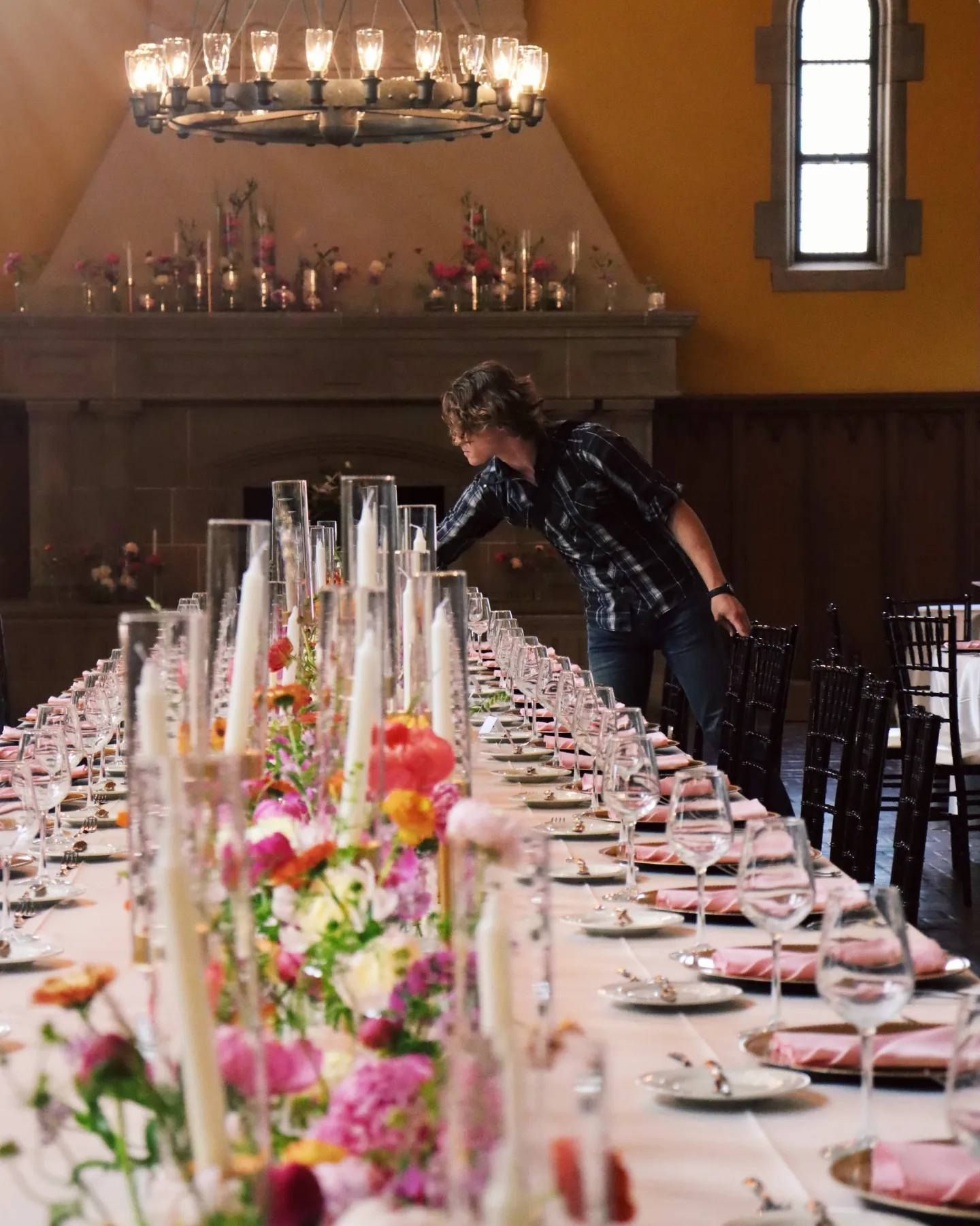A man is setting a long table with flowers and candles