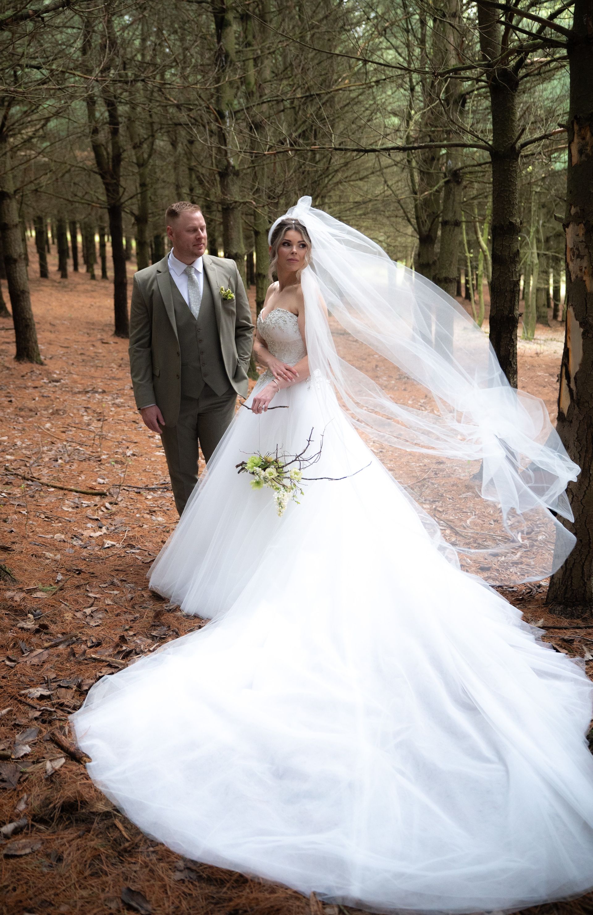 A bride and groom are posing for a picture in the woods.
