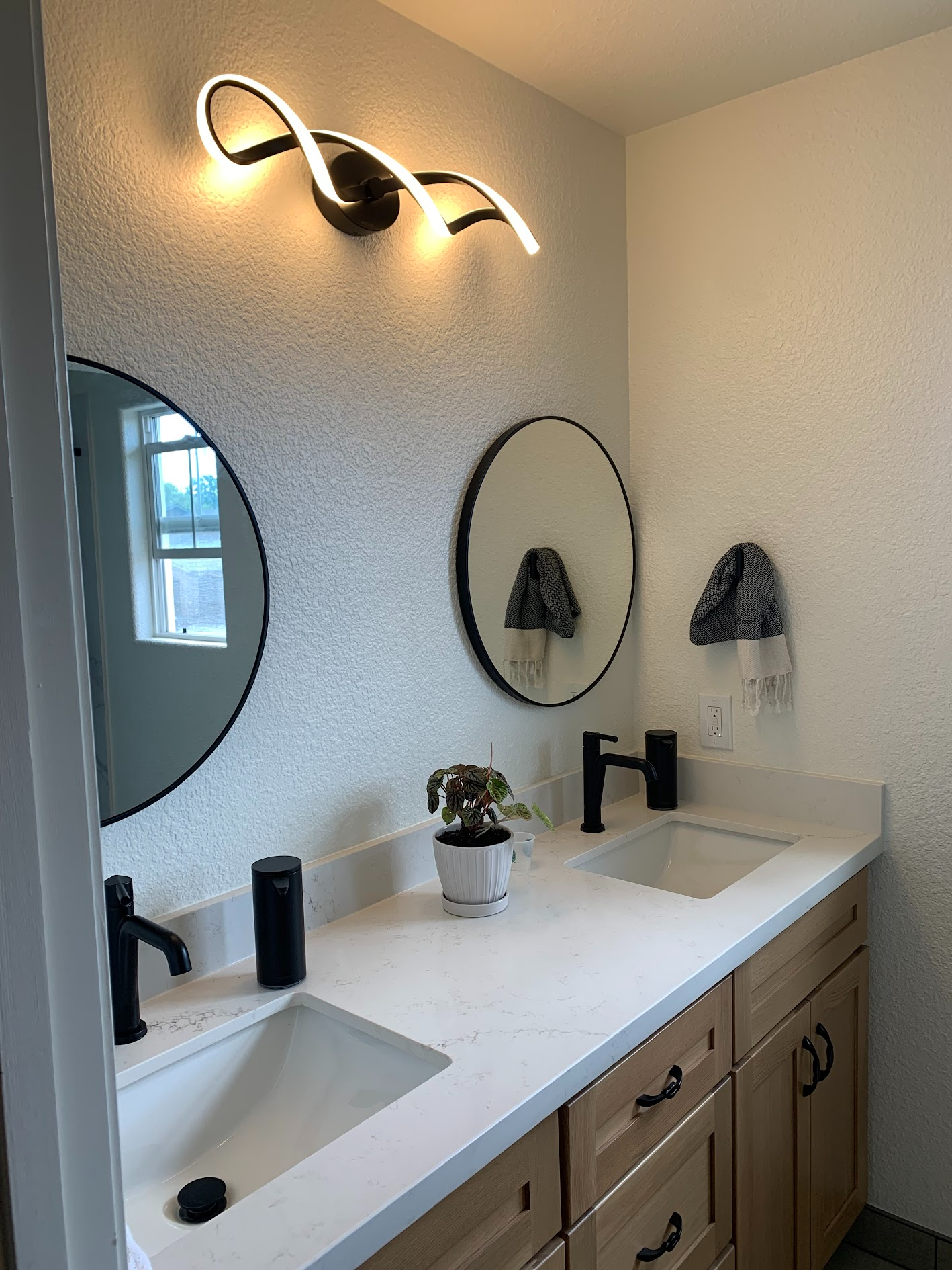 Modern bathroom vanity with white countertop, black fixtures, round mirror, and wall sconce lighting.