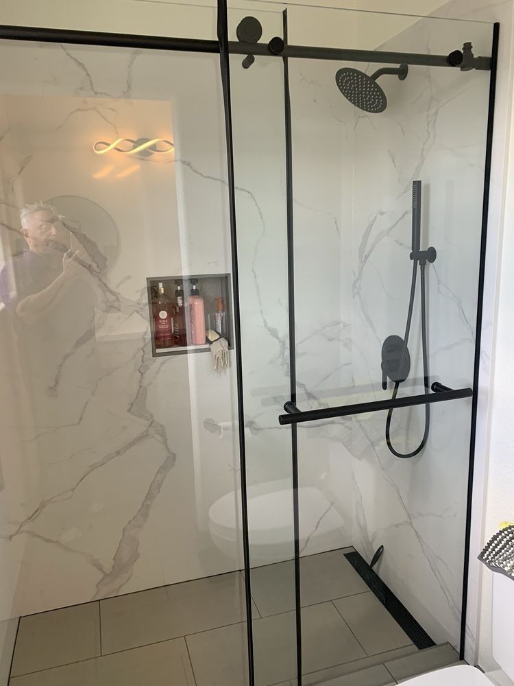 Glass-enclosed walk-in shower with marble-look walls, black fixtures, and tiled floor