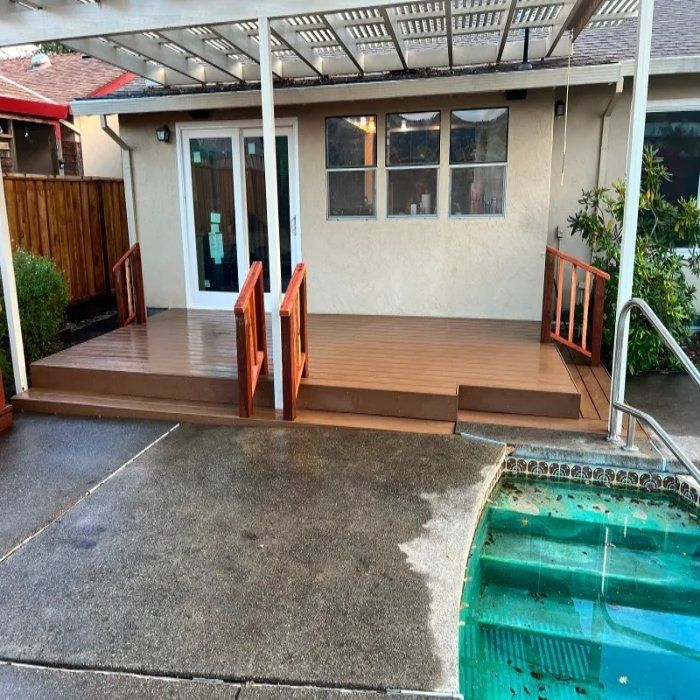 Covered patio and poolside deck with white doors, wooden railings, and wet concrete walkway